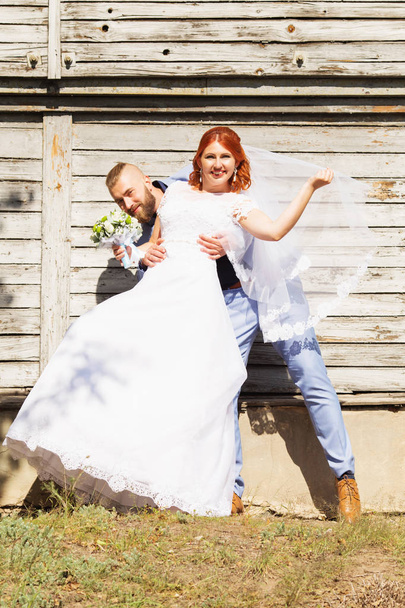 Just married loving hipster couple in wedding dress and suit posing in front of an old wooden house. Happy bride and groom walking running and dancing. Romantic Married young family. Autumn wedding - Photo, Image