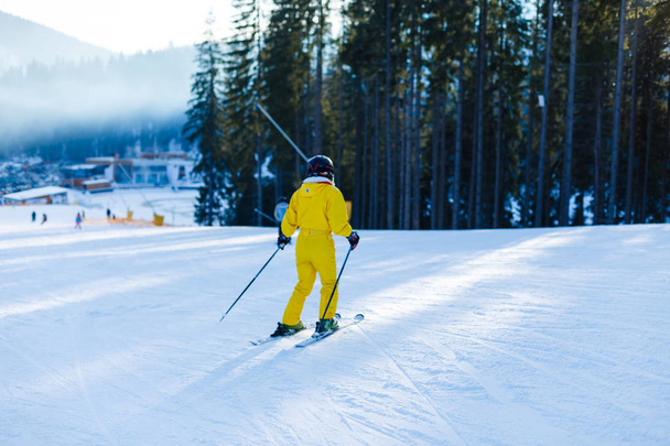 Woman in yellow winter jumpsuit riding skis in snowy mountains  - 写真・画像