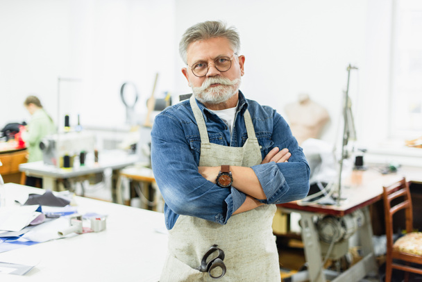 hombre maduro serio artesano en delantal posando con los brazos cruzados en el taller
 - Foto, Imagen