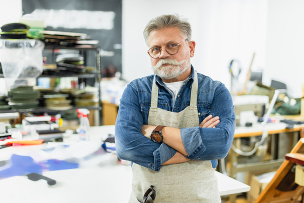 homme mature artisan dans tablier posant avec les bras croisés à l'atelier
 - Photo, image
