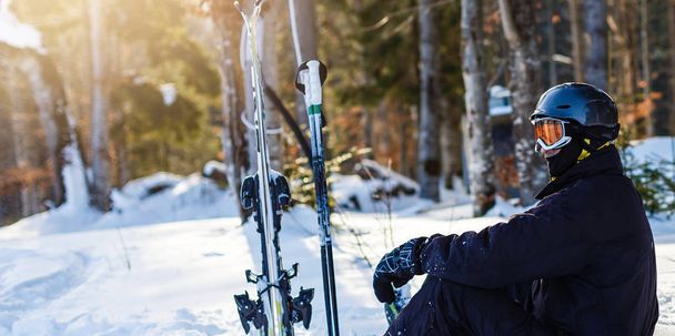 Gelukkige man in zwarte skiën pak rusten op witte sneeuw - Foto, afbeelding