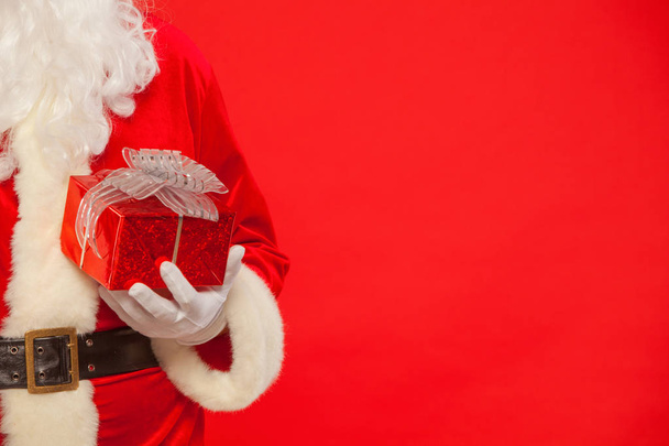 Photo of Santa Claus gloved hands holding red giftbox - Foto, afbeelding