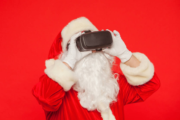 Santa Claus wearing virtual reality goggles, on a red background - 写真・画像