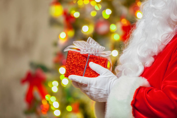 Santa Claus with giftbox on background of sparkling firtree - Zdjęcie, obraz