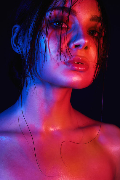Χρώμα που λάμπει το πρόσωπό του ένα κορίτσι. Ουράνιο τόξο γυναίκα σε πολύχρωμα φωτεινά φώτα στο studio. Τέχνη σχεδιασμού, πολύχρωμα κορίτσι με βρεγμένα μαλλιά - Φωτογραφία, εικόνα