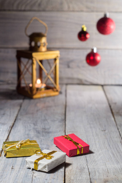 Linterna con una vela y decoraciones navideñas: bolas y cajas sobre una superficie de madera blanca
 - Foto, Imagen