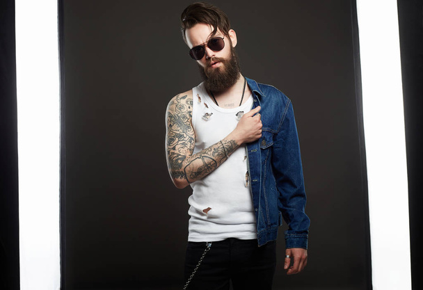 fashionable handsome man with tattoo and sunglasses. Hipster bearded Stylish boy in jeans and glasses - Photo, Image