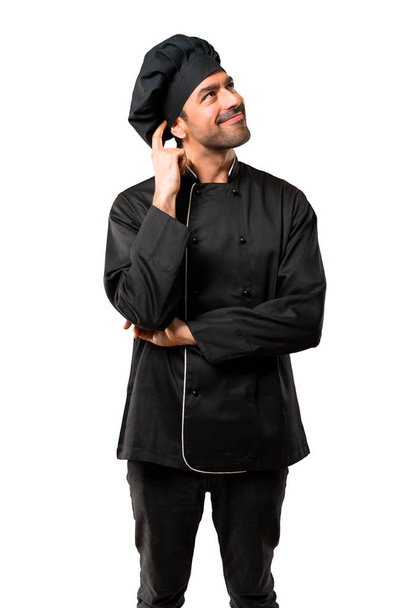 Kuchař muž v černé uniformě stál a přemýšlel myšlenka při poškrábání hlavu na izolované bílém pozadí - Fotografie, Obrázek