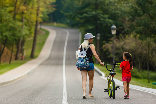 молода мати і її дочка катаються на велосипеді в парку
 - Фото, зображення