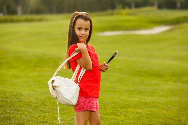 緑のゴルフ場で楽しみを持っている小さなブルネットの女の子  - 写真・画像