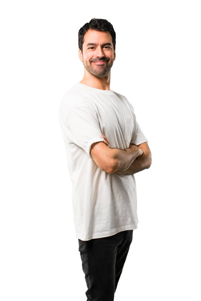 Young man with white shirt keeping the arms crossed in lateral position while smiling. Confident expression on isolated white background - Zdjęcie, obraz