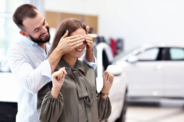 Hombre adulto haciendo sorpresa a hermosa mujer en sala de exposición de coches
 - Foto, imagen