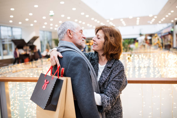 Happy senior couple with paper bags in shopping center, hugging. - 写真・画像