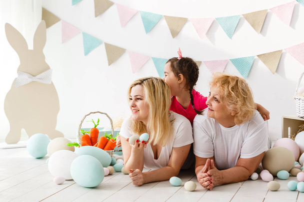 Happy little girl with mother and grandmother playing with Easter eggs - Fotografie, Obrázek