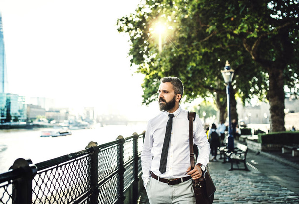 Hipster businessman with laptop bag walking by the river in London. - Foto, Imagen