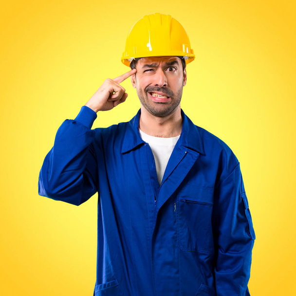 Young workman with helmet making the gesture of madness putting finger on the head on yellow background - Photo, Image