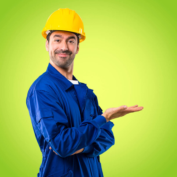Nuori työmies kypärä esittää tuotteen tai idean hymyillen kohti vihreää taustaa
 - Valokuva, kuva