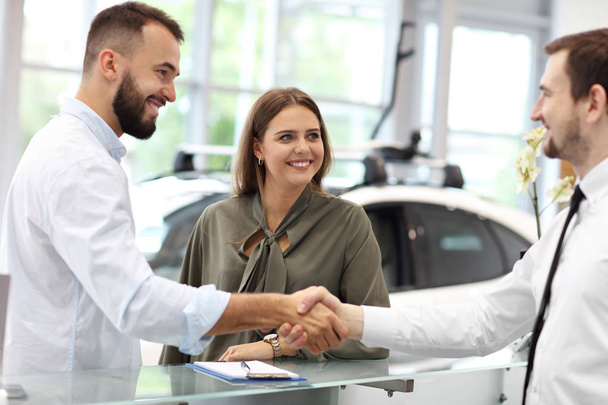 Confident young salesman explaining car features to the young attractive owners - Photo, Image