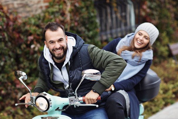 秋の市でスクーターに乗りながら笑みを浮かべて美しい若いカップル - 写真・画像