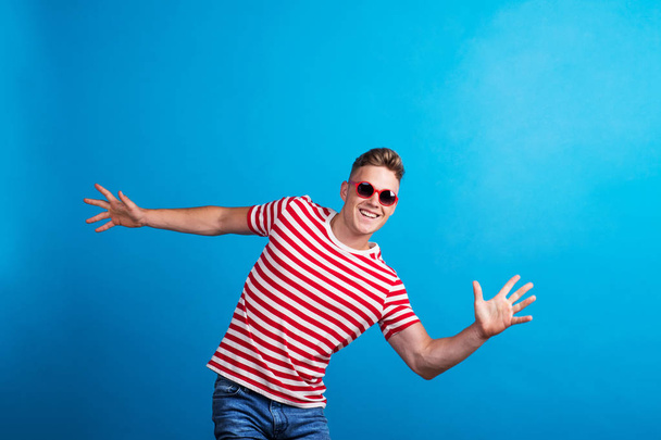 A young man with red sunglasses standing in a studio, having fun. - Foto, Bild