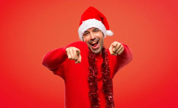 Człowiek z czerwone ubrania obchodzi Boże Narodzenie wakacje punktów palec na Ciebie jednocześnie uśmiechając się na czerwonym tle - Zdjęcie, obraz