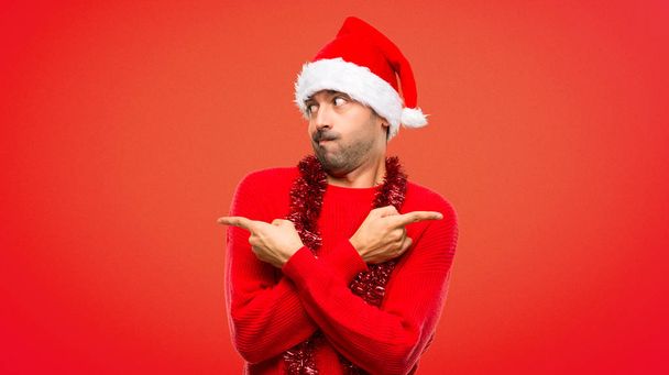 Mies punaisissa vaatteissa juhlii joululomaa osoittaen lateraleihin, joilla on epäilyksiä punaisesta taustasta
 - Valokuva, kuva