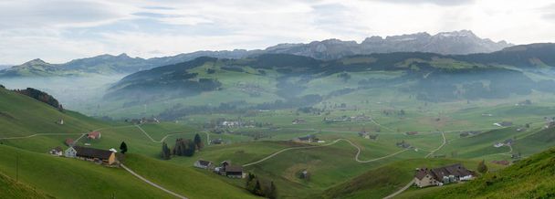 panorama landscape view of the beautiful Appenzell region in Switzerland with ist rolling hills and farms and the Alpstein mountains behind and a lone hiker admiring the view - Photo, Image
