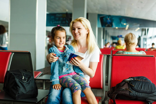 Νεαρή μητέρα και κόρη περιμένουν για αναχώρηση στην αίθουσα αναμονής του αεροδρομίου - Φωτογραφία, εικόνα