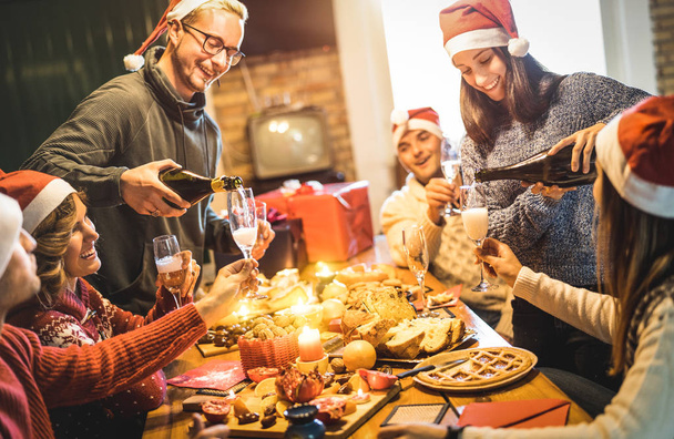 Групи друзів з Санта капелюхів, святкування Різдва з шампанське і цукерки продукти харчування на Дом вечеря - зимові свята концепції з людьми, насолоджуючись часу і весело разом їдять - теплий фільтр - Фото, зображення