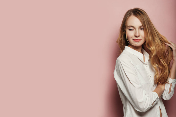 Portrait of pretty Caucasian woman with long hair, wearing a white shirt on pink background - Fotografie, Obrázek