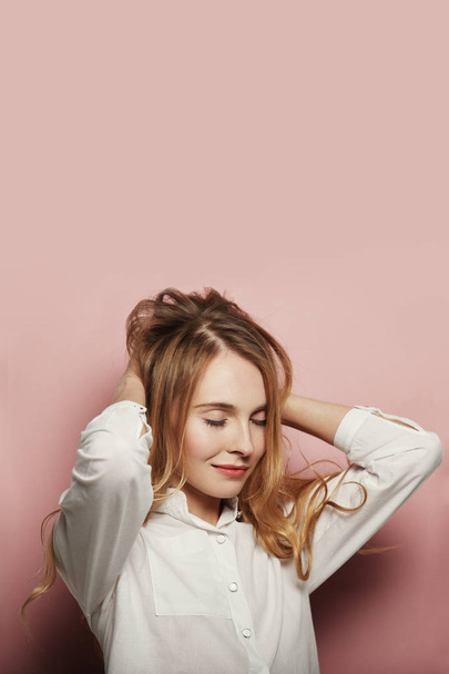 Портрет красивой белой женщины с длинными волосами, в белой рубашке на розовом фоне
 - Фото, изображение
