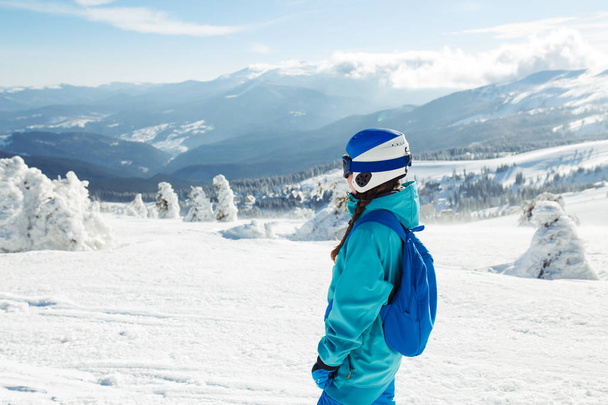 A beautiful girl in winter clothes, a blue helmet and a green jacket is having a great time in the mountains. Concept of travel, leisure, freedom, sport. Beautiful nature, places, great weather.  - Foto, Imagem