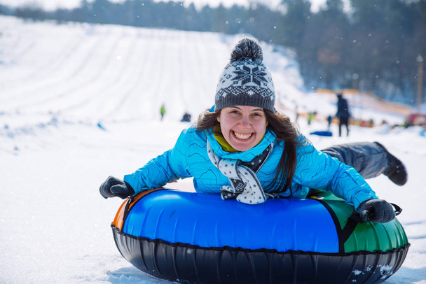jong lachend meisje rijden slee sneeuw tubing heuvel winter activiteit concept - Foto, afbeelding