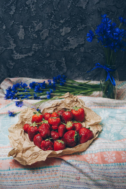 Seasonal summer flowers in vase blue cornflowers and fruits strawberries on a napkin close-up conceptual background - Photo, Image
