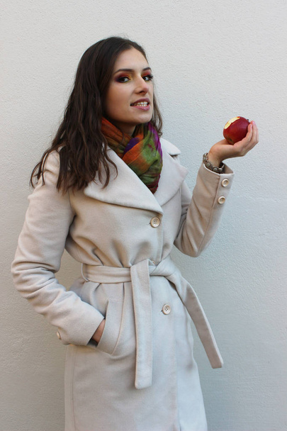 woman in a coat holding a bitten red juicy apple - Foto, afbeelding