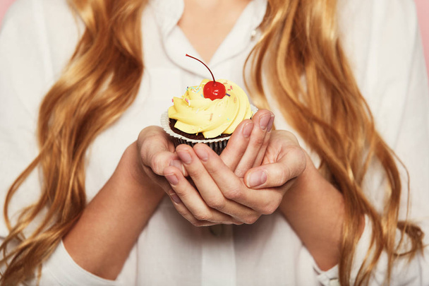 Mulher mãos segurando um delicioso cupcake com uma cereja em cima, close-up
. - Foto, Imagem