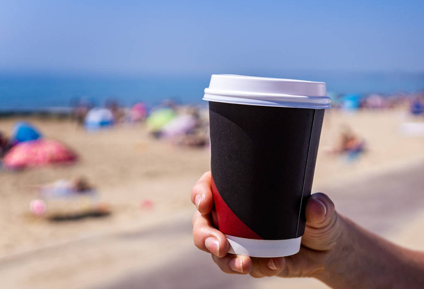 Close up de copo de café descartável sendo realizada contra um fundo de praia
 - Foto, Imagem