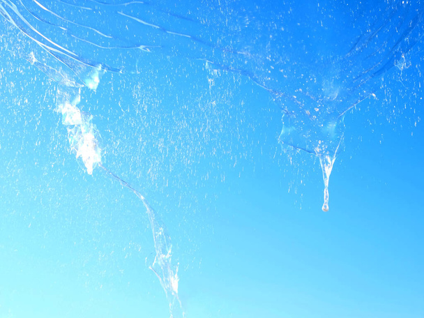 Велика бульбашка, що вибухає в небі, яскраво-блакитна позаду, вибухова бульбашка прозора, але відображає кольори неба позаду
 - Фото, зображення