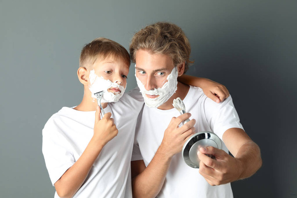 Father and son shaving together on color background - 写真・画像