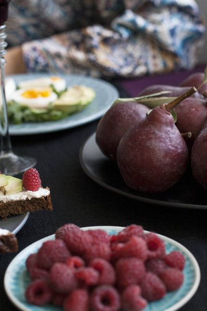 Легкий летний ужин на двоих: вареные яйца с рукколой и авокадо, малина на десерт, фиолетовые груши и белое вино
. - Фото, изображение