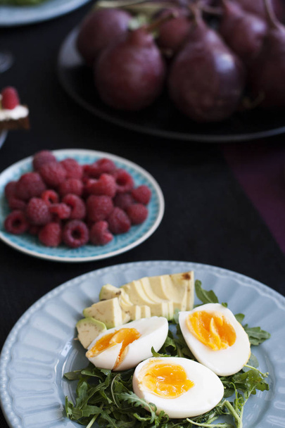 Ένα ελαφρύ καλοκαιρινό γεύμα για δύο: βραστά αυγά με ρόκα και αβοκάντο, τα σμέουρα για επιδόρπιο, μοβ, λευκό κρασί και αχλάδια. - Φωτογραφία, εικόνα