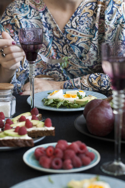 Una cena ligera de verano para dos personas: huevos cocidos con rúcula y aguacate, frambuesas de postre, peras moradas y vino blanco
. - Foto, Imagen