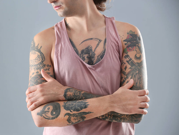 Young man with stylish tattoos on grey background - Фото, изображение