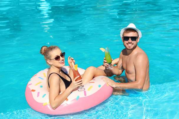 Young couple with refreshing cocktails and inflatable ring in swimming pool - Foto, Imagen
