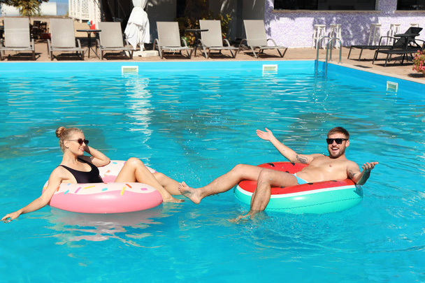 Happy young couple with inflatable rings in swimming pool - Photo, Image