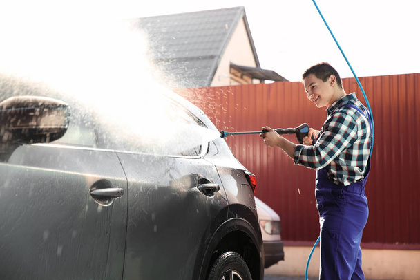 Worker cleaning automobile with high pressure water jet at car wash - Фото, зображення