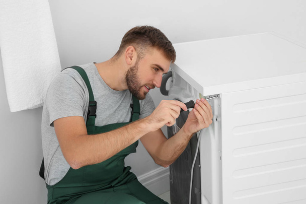Young plumber fixing washing machine in bathroom - Foto, immagini