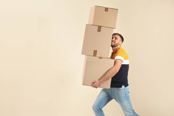 Portrait of young man carrying carton boxes on color background. Posture concept - Fotó, kép