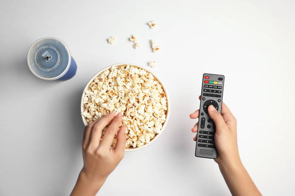 Woman with TV remote eating popcorn on white background, top view. Watching cinema - Фото, зображення
