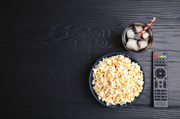 Bowl with popcorn, glass of iced cola and TV remote on wooden background, top view with space for text. Watching cinema - Foto, imagen